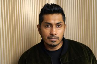 Tenoch Huerta poses in a dark green velvet jacket and black shirt against a gold background.