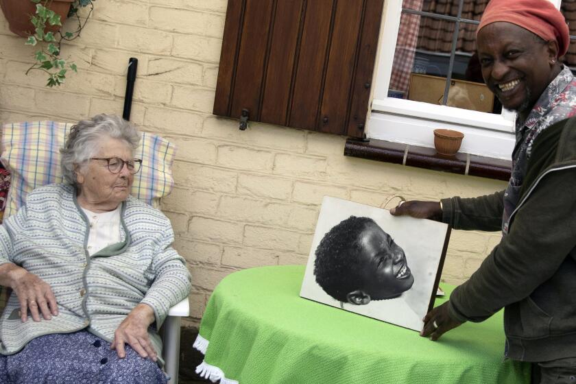 In this photo taken on Monday, June 22, 2020, Eric Baranyanka, right, and his foster mother Emma Monsaert look at a photo of Eric as a young boy in Lembeek, Belgium. Baranyanka fled political persecution in the Belgian protectorate of Burundi in the 1960's, landing half a world away at a military airport in Brussels, before being fostered by Emma Monsaert and her husband Paul. (AP Photo/Virginia Mayo)