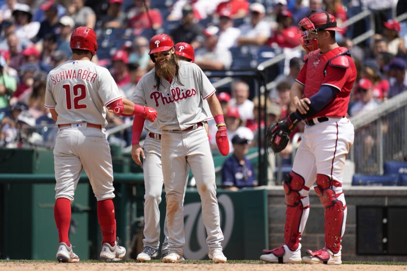 Philadelphia Phillies' Kyle Schwarber (12) celebrates with teammates Brandon Marsh and Drew Ellis after batting them in on a home run in front of Washington Nationals catcher Riley Adams, right, in the sixth inning of a baseball game, Sunday, June 4, 2023, in Washington. (AP Photo/Patrick Semansky)