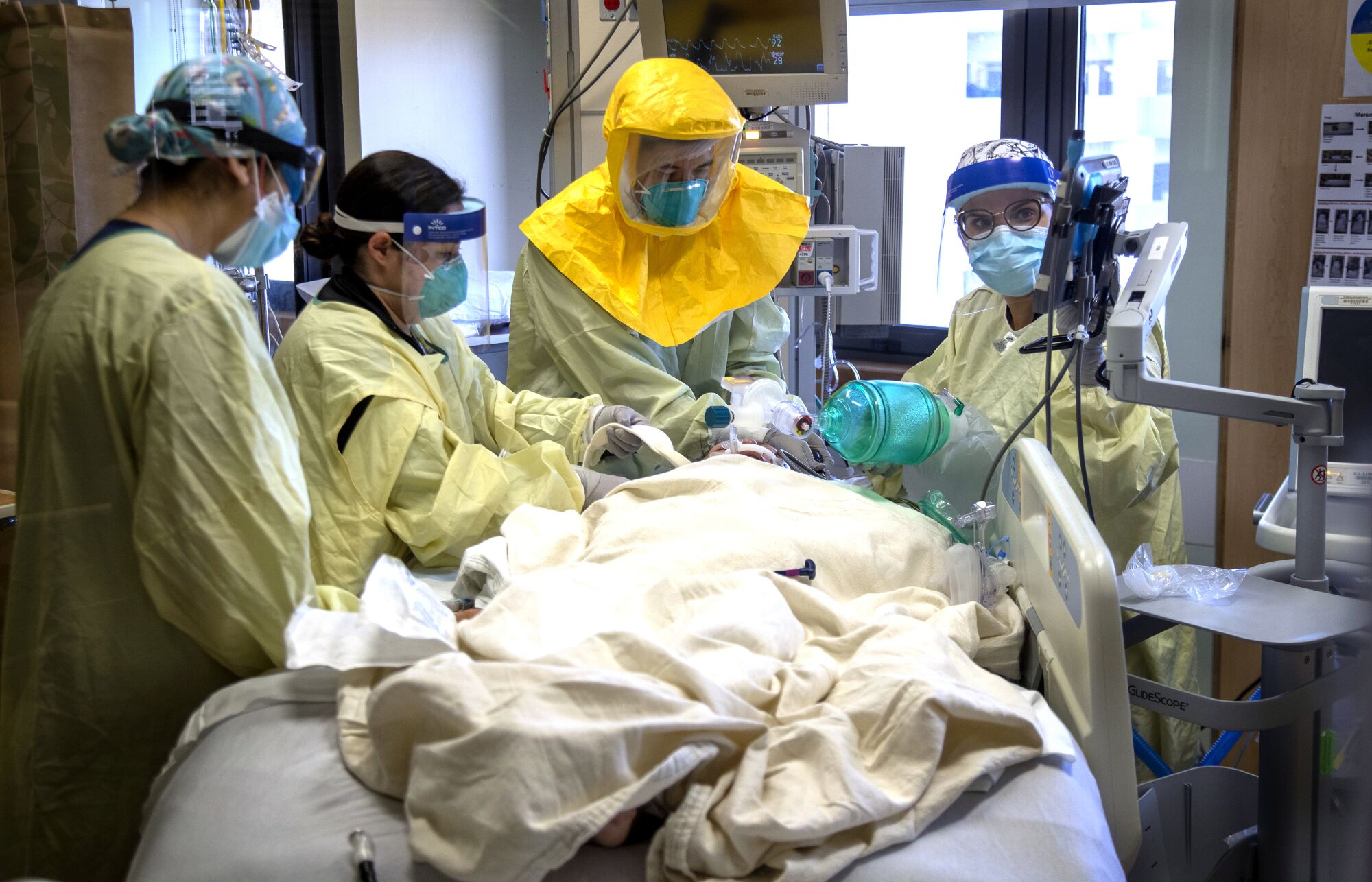 Hospital staff in protective masks, gowns and face shields work on a person lying on a hospital bed.