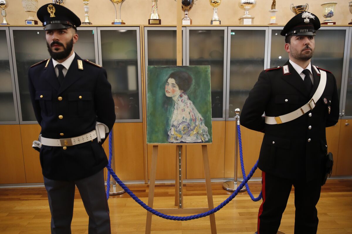 FILE - In this Friday, Jan. 17, 2020 file photo, an Italian Policeman, left, and a Carabiniere, paramilitary police officer, stand beside a painting which was found last December near an art gallery and believed to be the missing Gustav Klimt's painting 'Portrait of a Lady' during a press conference in Piacenza, Italy. Gustav Klimt's "Portrait of a Lady," which was missing for nearly 23 years after its theft from an Italian museum, will be a star in an exhibit about the artist that is opening this month at a Rome museum. (AP Photo/Antonio Calanni)