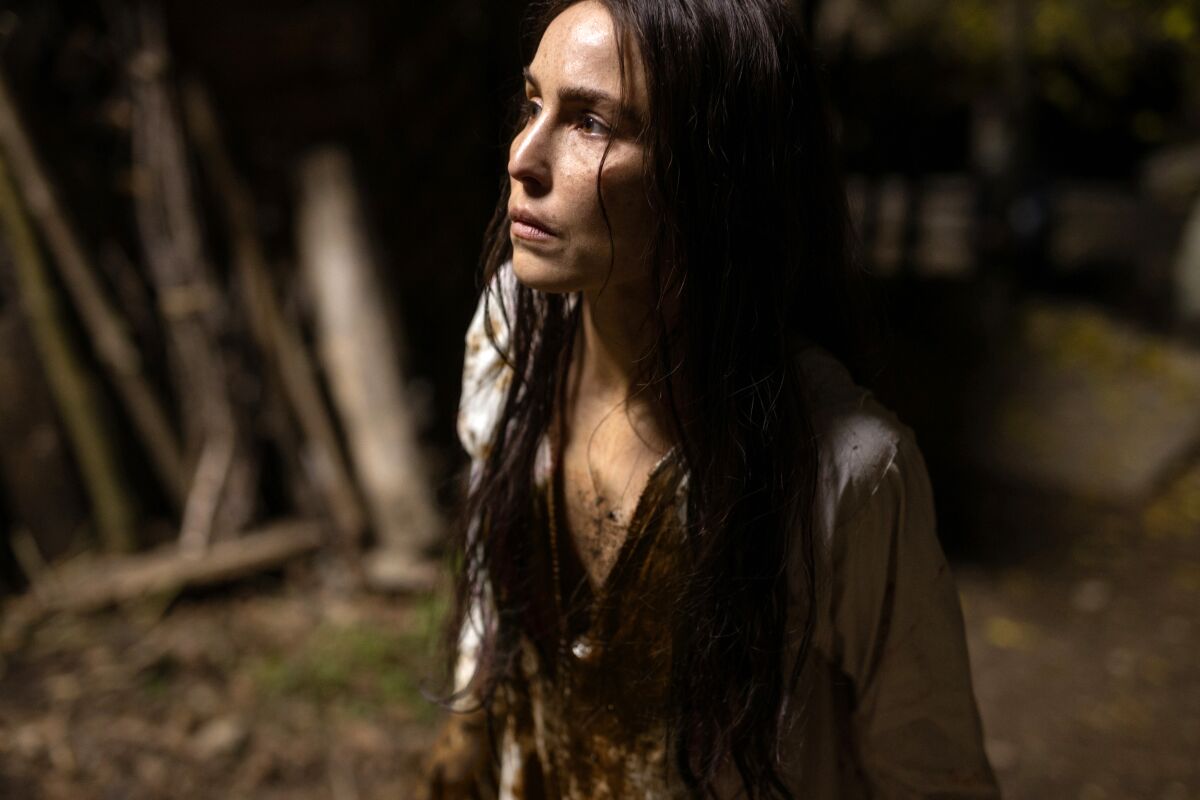Closeup of a woman with long dark hair and dirt on the front of her clothes.