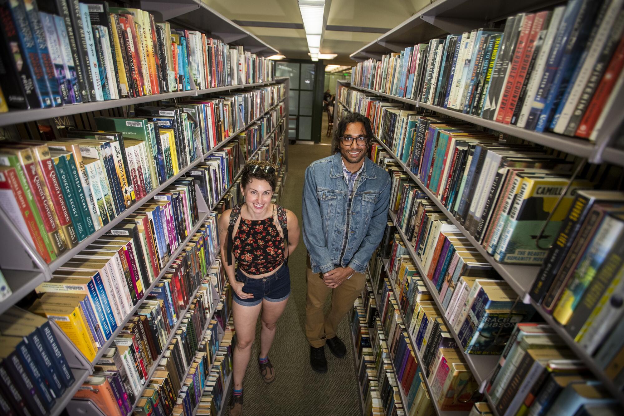A man and a woman smile amid rows of books in a library.