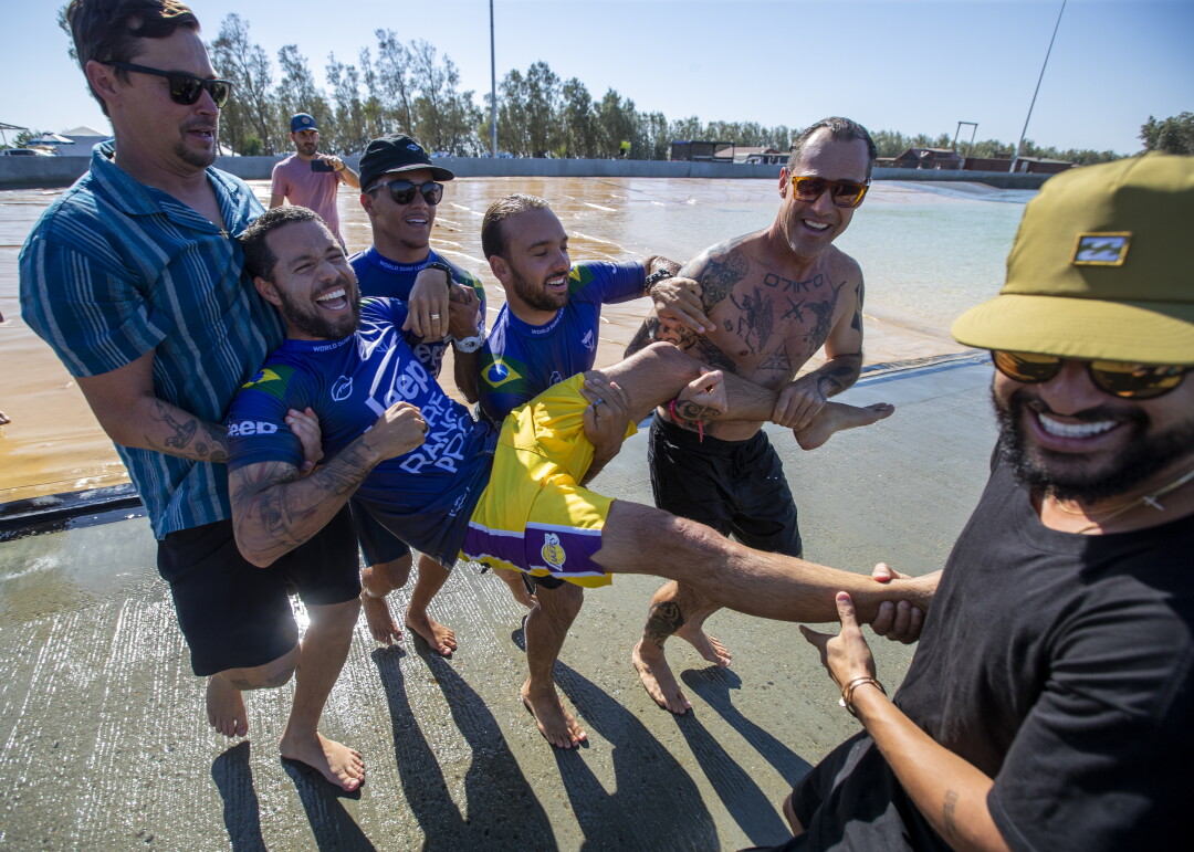 Des amis emmènent le surfeur Adriano de Souza dans l'eau.