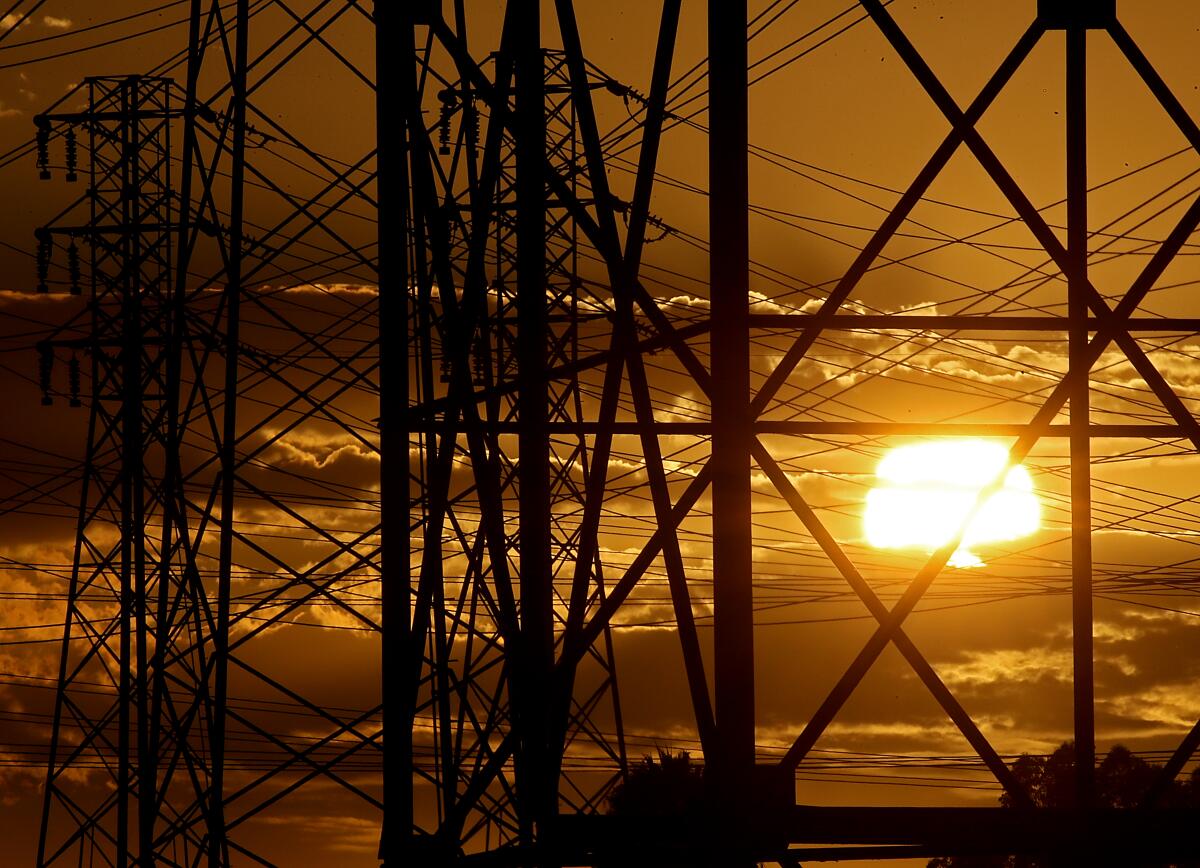 The setting sun is seen amid clouds and behind crisscrossing power lines.