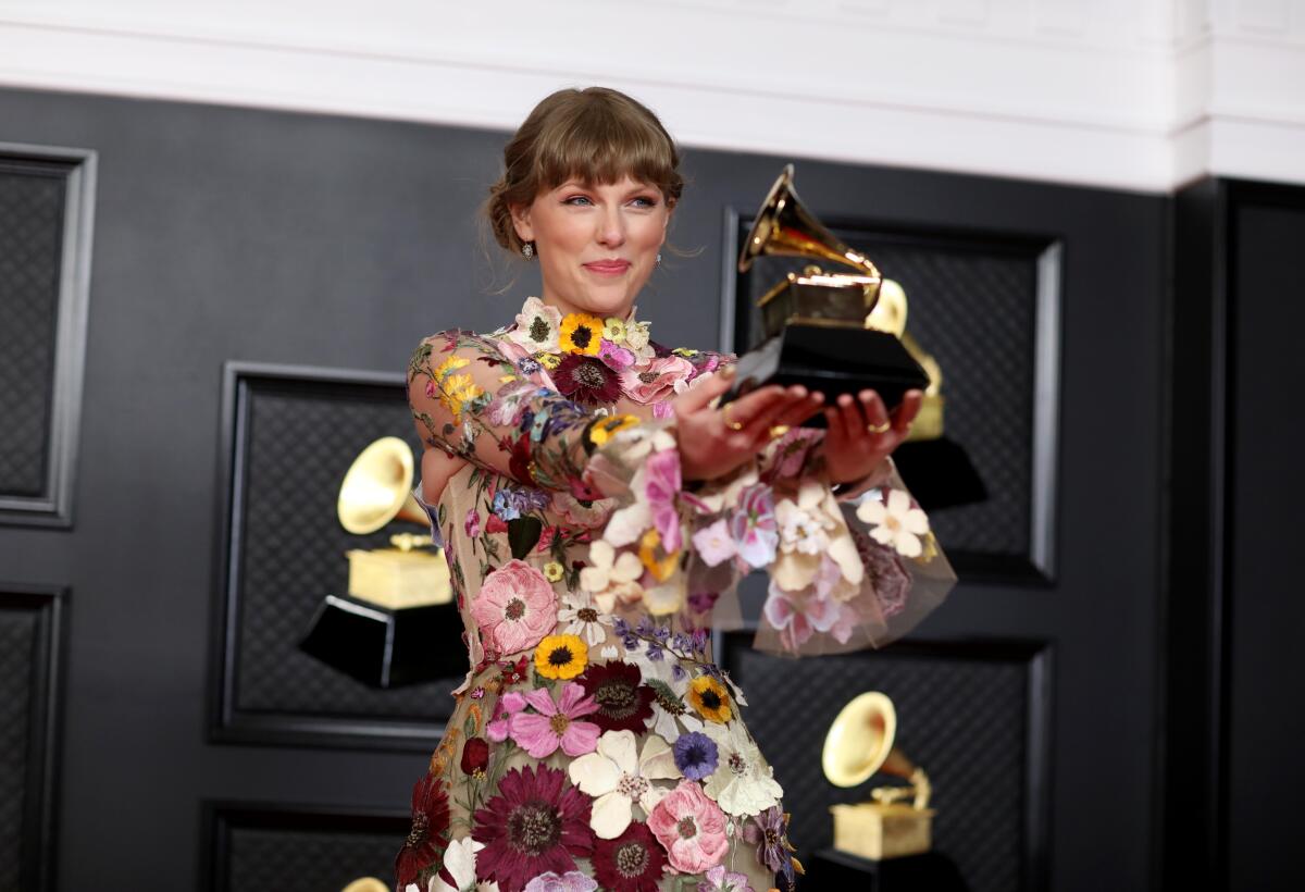 Taylor Swift holds her Grammy trophy on a red carpet