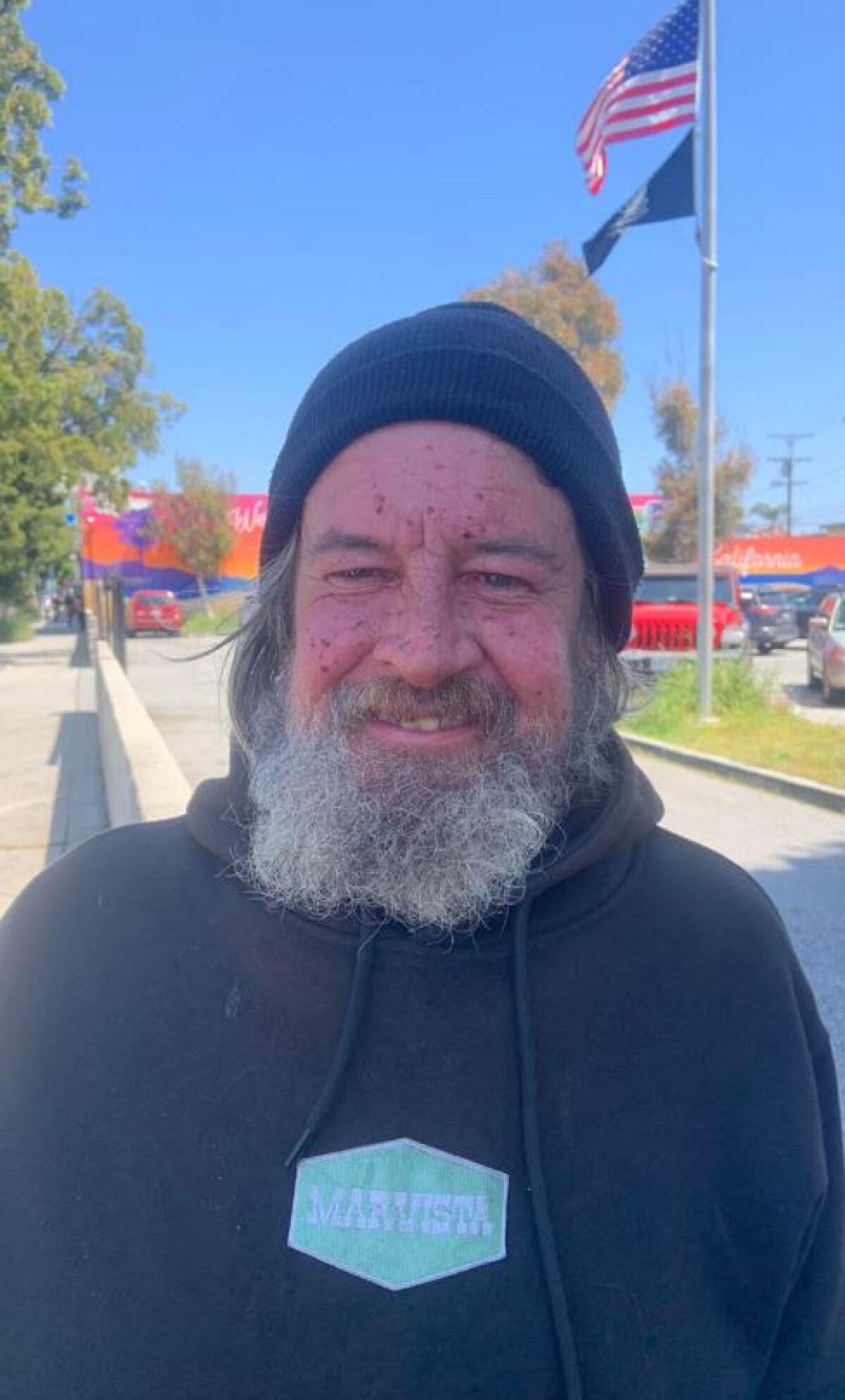 A man with a gray beard and a stocking cap stands outdoors