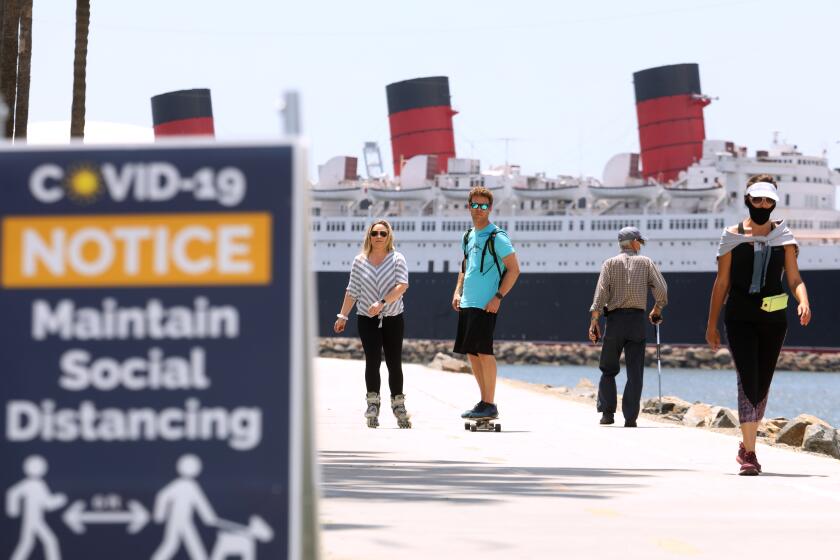 LONG BEACH, CA - MAY 11, 2020 - - Scially distanced bikers and walkers, against a backdrop of the Queen Mary, make their way along pedestrian and beach bike path on the first day that Long Beach reopened the path on Monday May 11, 2020. The city of Long Beach eased a few of its public health restrictions, allowing under certain guidelines the reopening of pedestrian and beach bike paths, tennis centers and courts. Beach bathrooms are also reopening, but the parking lots and beaches still remain closed. (Genaro Molina / Los Angeles Times)