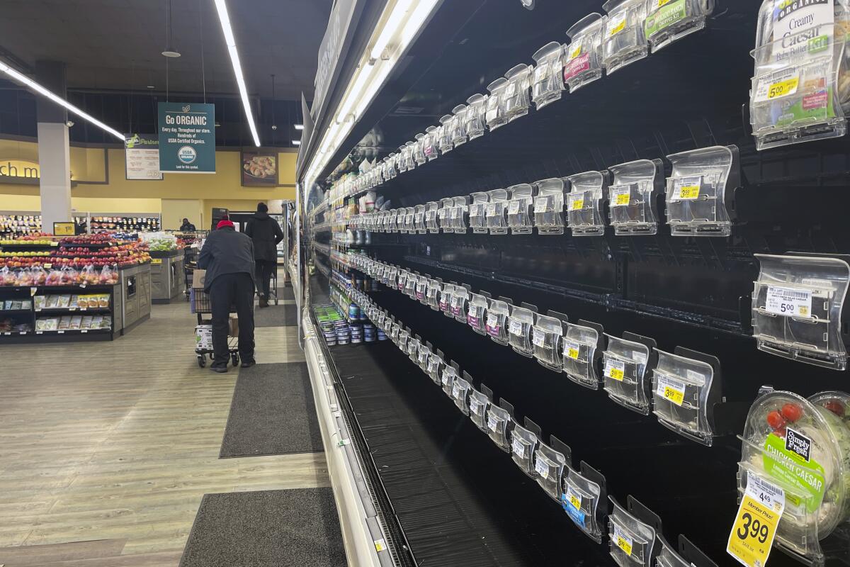 Unas personas caminan por pasillos con estantes vacíos en una tienda de Safeway, 