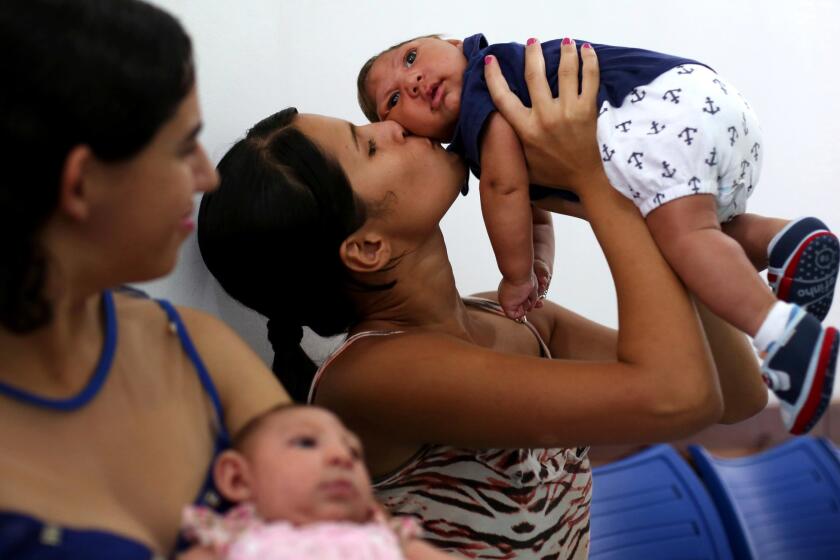 CAMPINA GRANDE, BRAZIL: March 14, 2016 - Kalissandra Matias de Olivera, age 17, kisses her son, Nicolas Felipe Alves de Olivera, 3 months, as Maria Carolina Silva Floa, age 20, looks on with her baby Maria Gabriela Silva Alves, 2 months, as they wait for their physiotherapy appointments at the Pedro I Municipal Hospital in Campina Grande, Brazil. Nicolas Felipe and Maria Gabriela were both born with microcephaly, and bring their children to the hospital for physiotherapy two times a week. Kalissandra found out that her child had microcephaly when he was born. She had never even heard of the birth defect, and was told to come to Pedro 1 and they would explain. She started bringing Nicolas Felipe to physiotherapy when he was 17 days old. (Katie Falkenberg / Los Angeles Times)