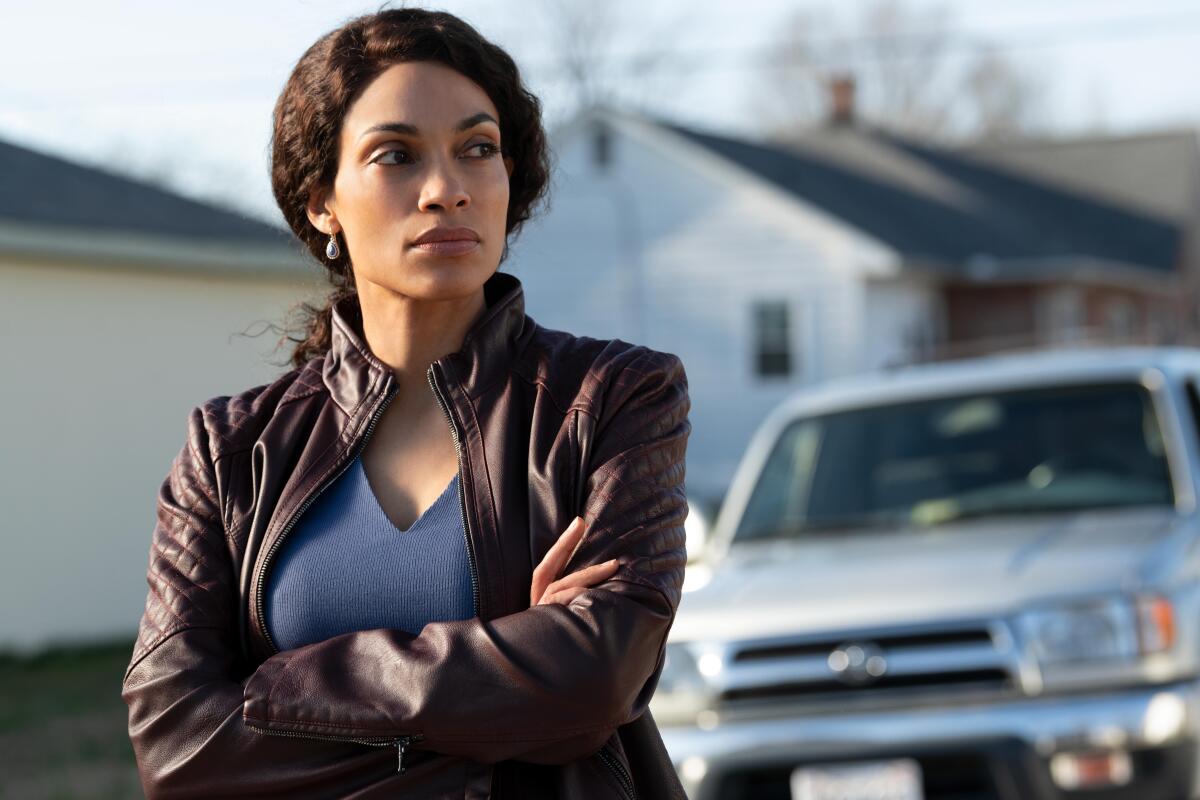 A woman stands in a rural street with her arms crossed