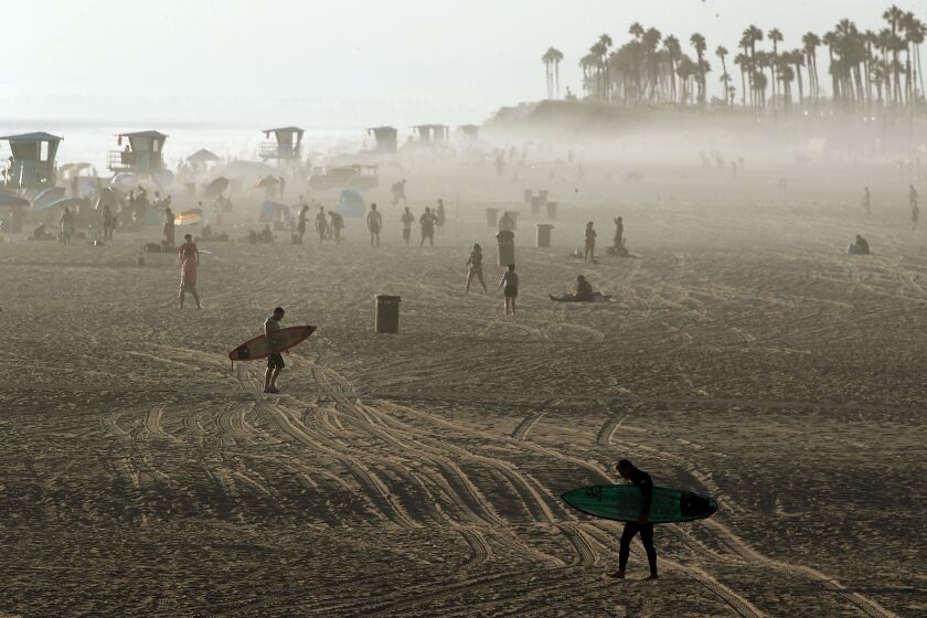 HUNTINGTON BEACH, CALIF. - SEP. 5, 2022. Surfers walk across the sand as fog driftys ashore at sunset at Huntington Beach on Monday, Sep. 5, 2022. (Luis Sinco / Los Angeles Times)