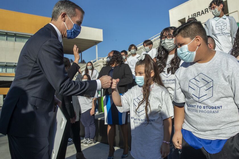 LOS ANGELES, CA-JANUARY 24, 2022: Los Angeles Mayor Eric Garcetti, left, greets Andrea Venegas, 7, and her brother, Andres Venegas, 9, after a press conference at Diego Rivera Performing Arts Community School in Los Angles, where he talked about the launching of Student 2 Student Success, a program providing economically disadvantaged students with job skills training and work experience. A total of 30 students at the school, including Andrea and Andres' sister Samantha Lira, 16, seen directly behind them, are participating in the program that teaches them how to do timesheets, write resumes, and tutor their siblings. They are getting paid $15 an hour and can work up to 1200 hours. The students must complete 20 hours of training with the mayor's office and from school counselor Steven Jabami, combined. (Mel Melcon / Los Angeles Times)