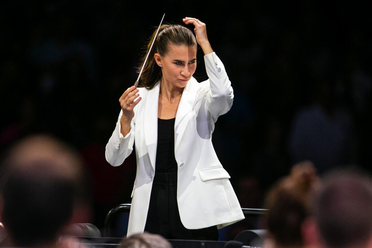 A woman wearing a white blazer holds a baton up with her other hand raised