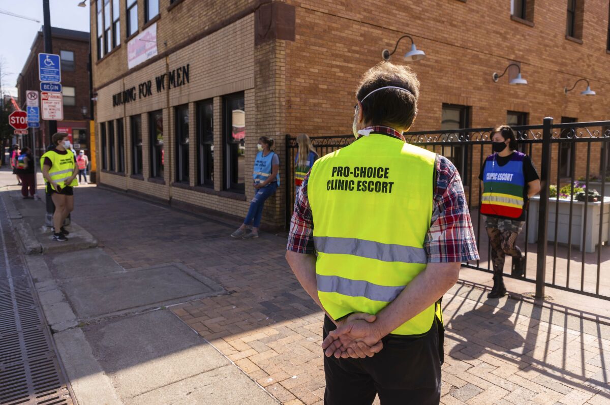 A clinic escort outside WE Health Clinic in Duluth, Minn., awaits the arrival of patients, Thursday, July 7, 2022. The clinic escorts protect patients from protesters as they approach and enter the clinic. (AP Photo/Derek Montgomery)