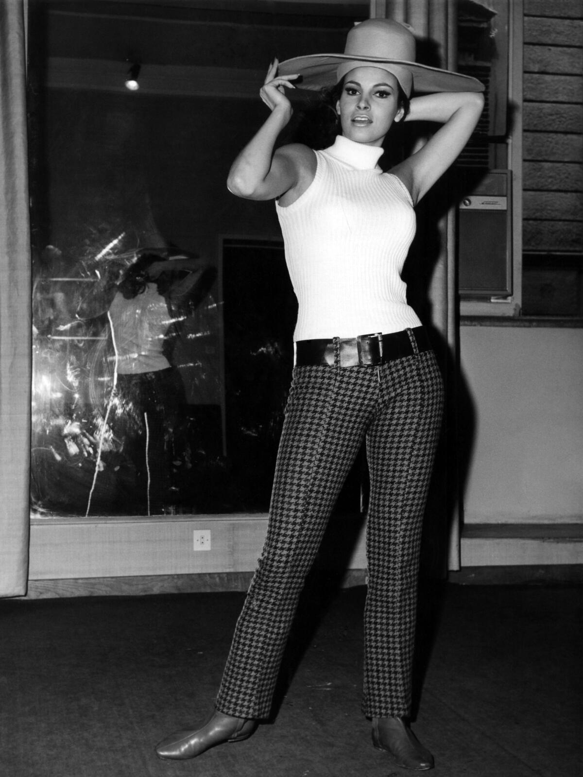 Woman wearing a wide-brimmed hat and white tank top turtle neck, plaid pants and boots in black and white photo