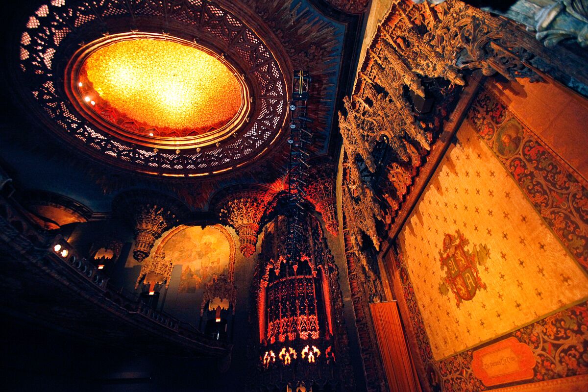A lighted ceiling dome above a stage proscenium on which Gothic ornamentation hangs like icicles.