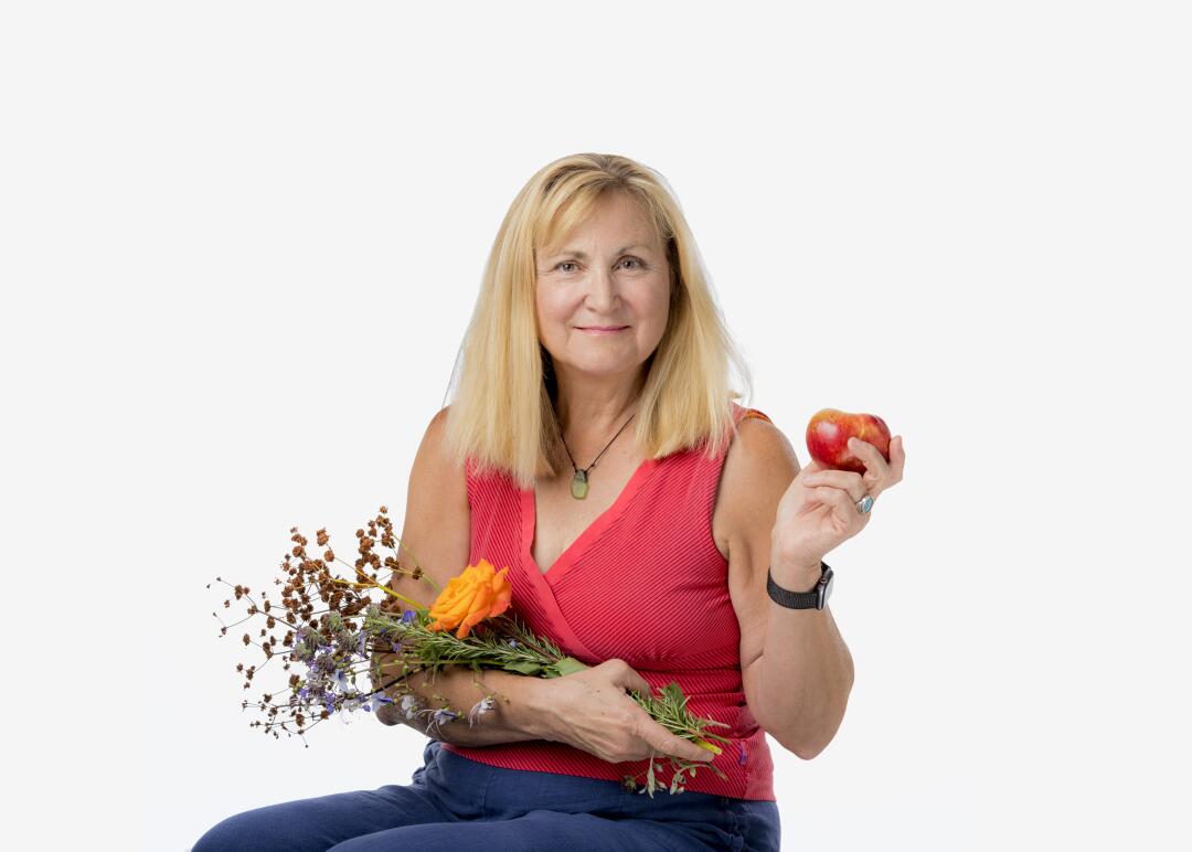 a woman holds flowers in one arm and a tomato in her other hand