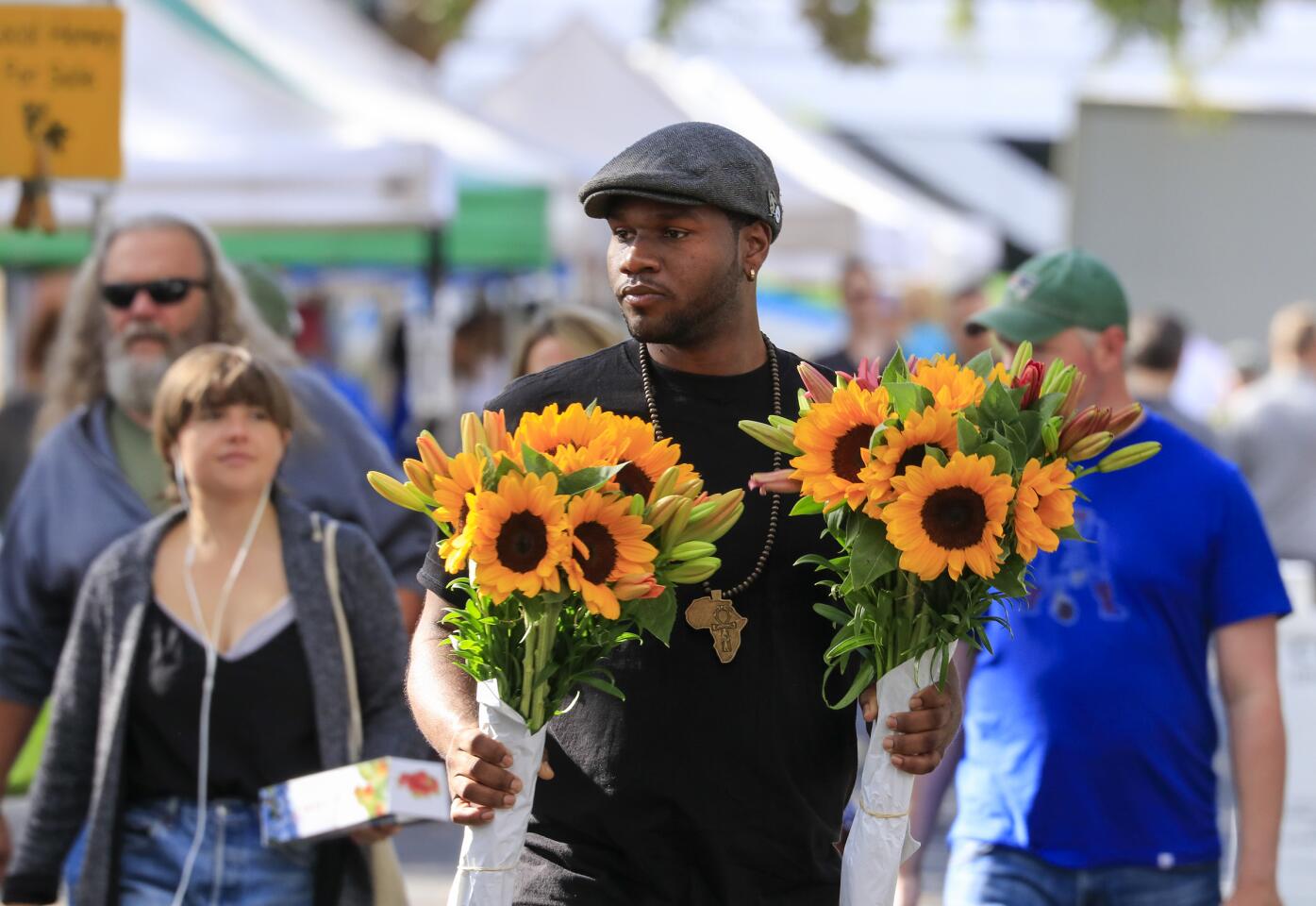 Customer Steven Russell carries two sunflower bouquets through the Claremont Farmers & Artisans Market in the heart of the Claremont Village in the city of Claremont.