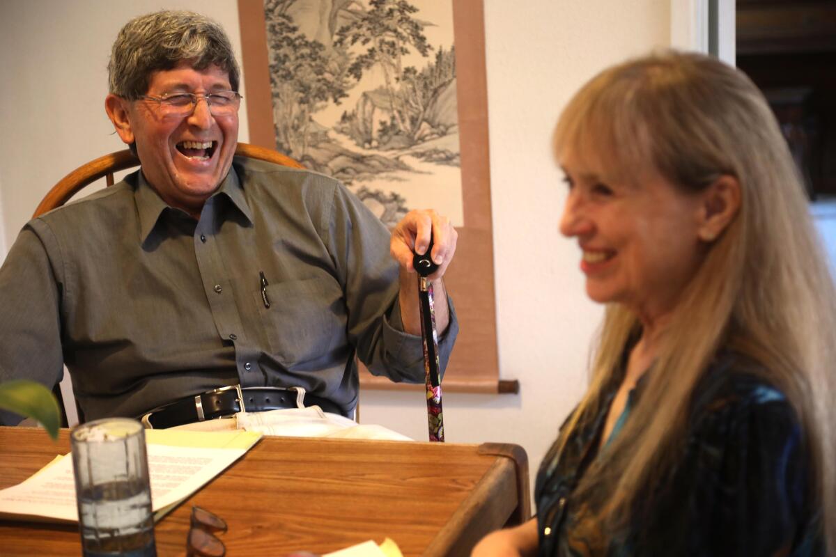 A man and woman laugh while sitting at a kitchen table