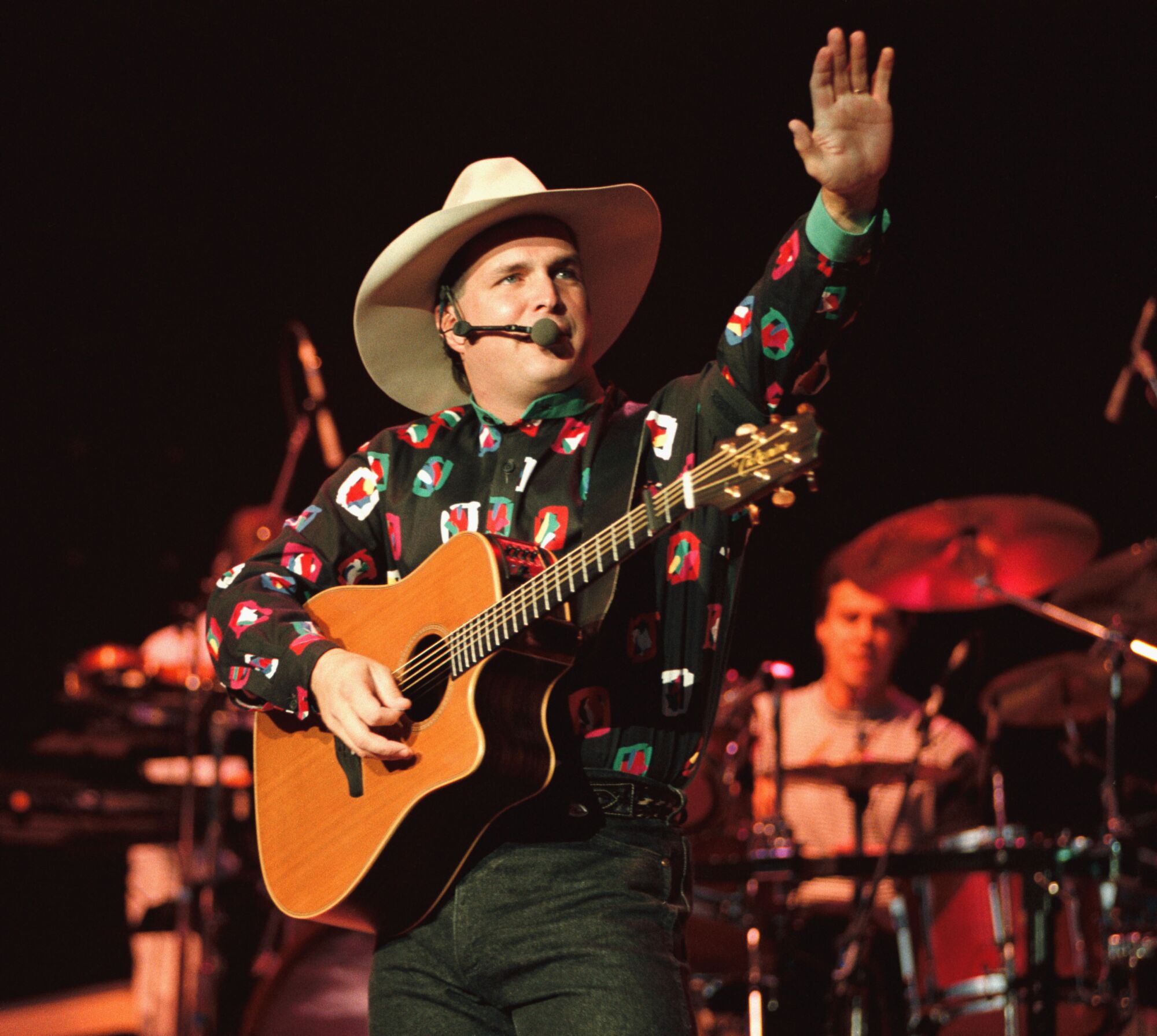 A man in a cowboy hat and holding a guitar waves from the stage