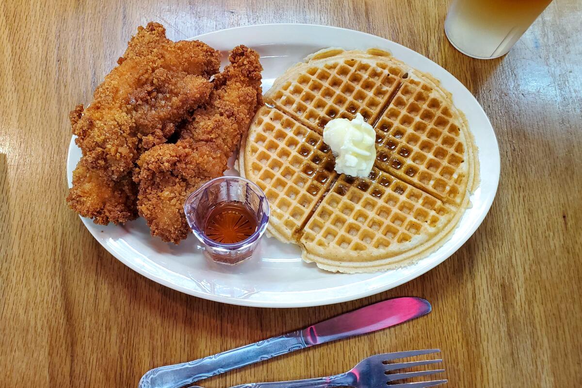 A waffle with a pat of butter and fried chicken tenders on a plate