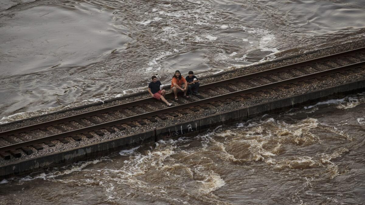 People sit on a railroad track near Lumberton, Texas, as floodwaters rush beneath them.