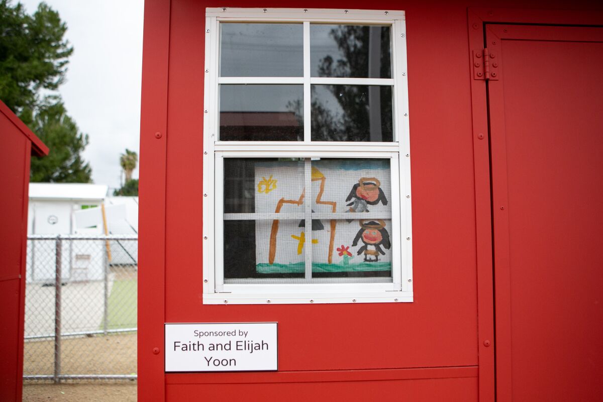 A child's painting of a house and a landscape decorates the window of a tiny home that is painted red