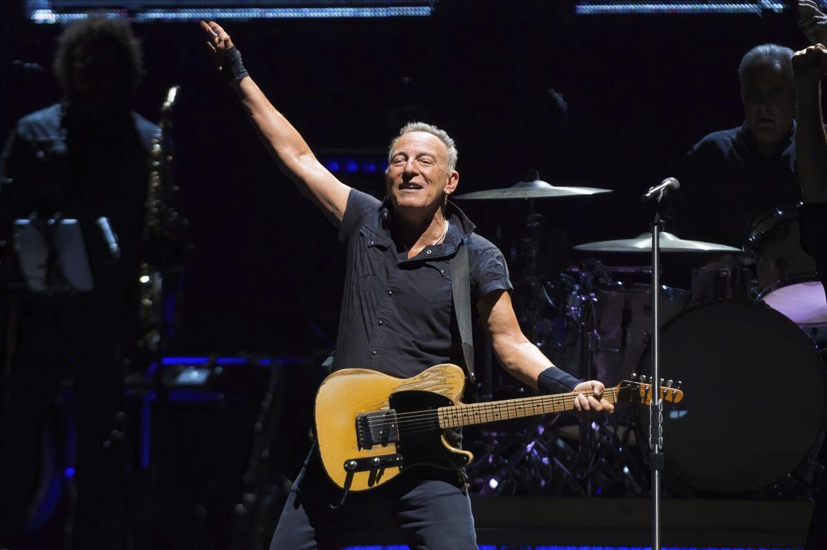 Bruce Springsteen wears a black polo and pants as he plays a maple Fender telecaster onstage