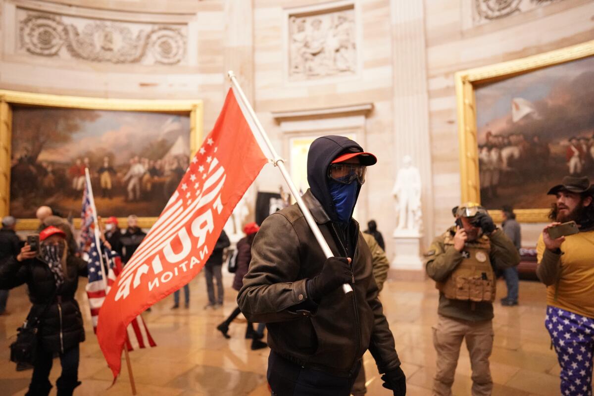 A man dressed all in black carries a red "Trump Nation" flag inside the Capitol Rotunda.