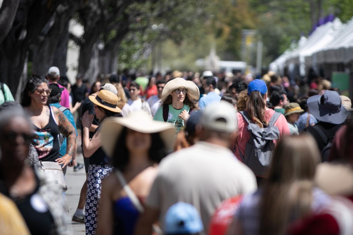 People walk on a sidewalk near popup tents at the Festival of Books