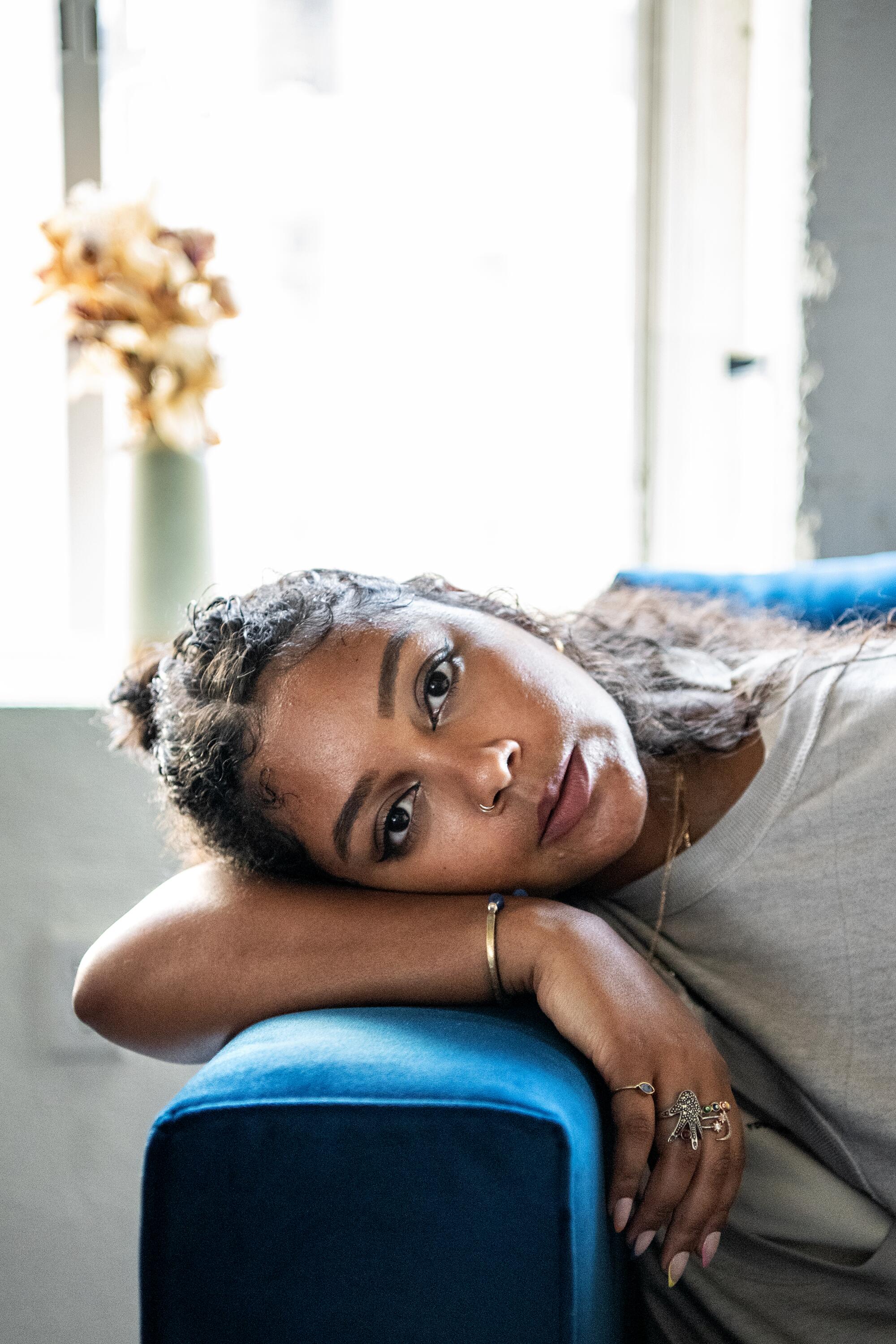 A woman leans on the arm of a couch