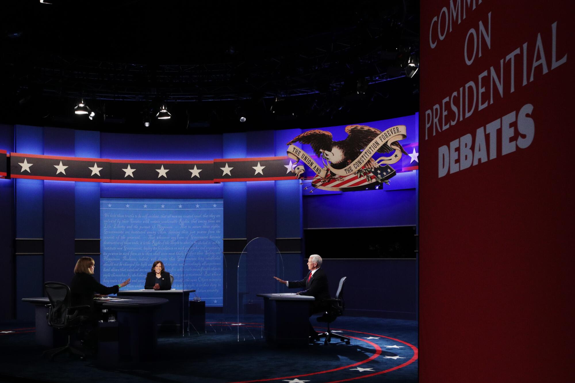 Moderator gestures as the candidates sit behind plexiglass onstage