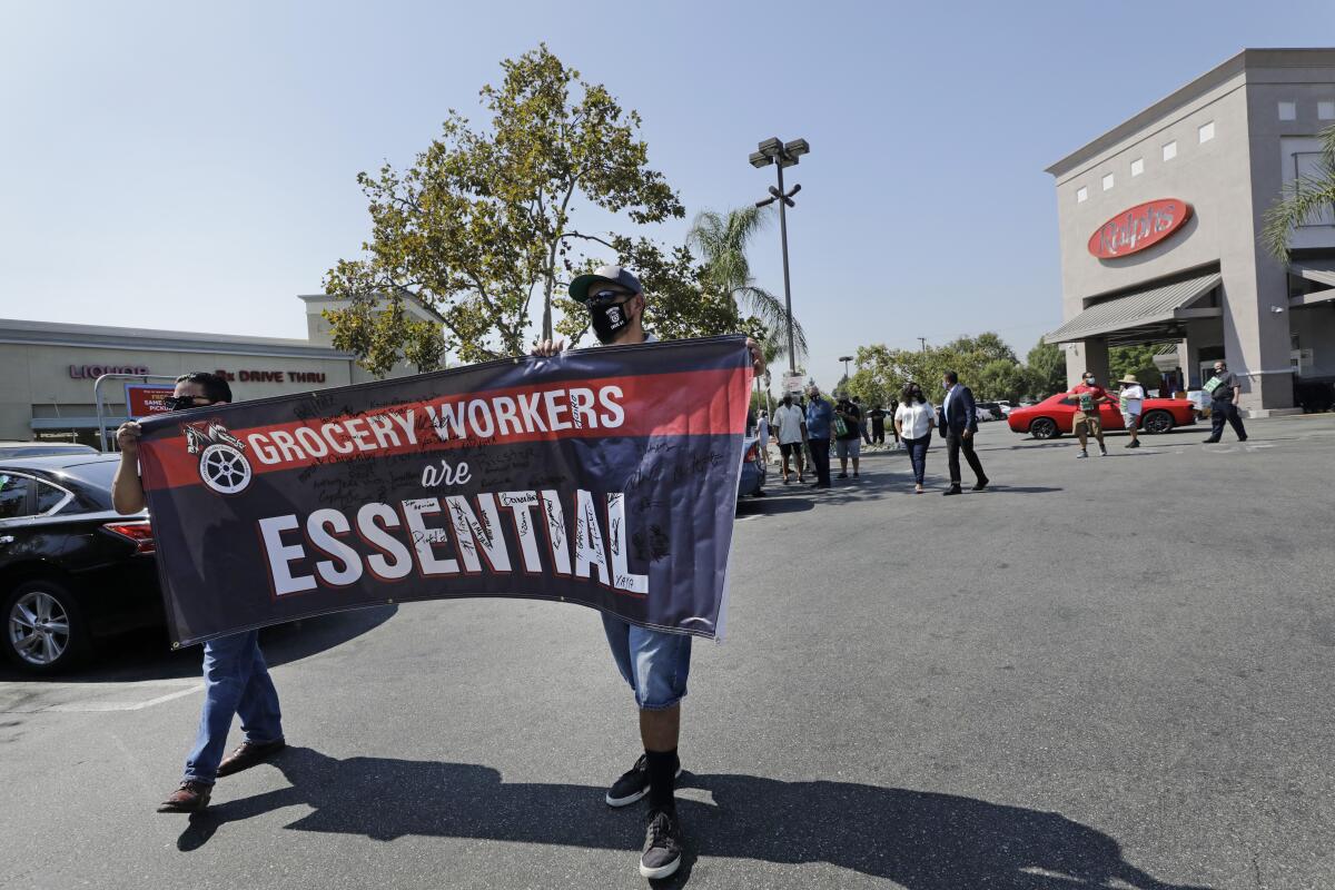 Two people hold up a banner that reads "Grocery Workers are Essential" 