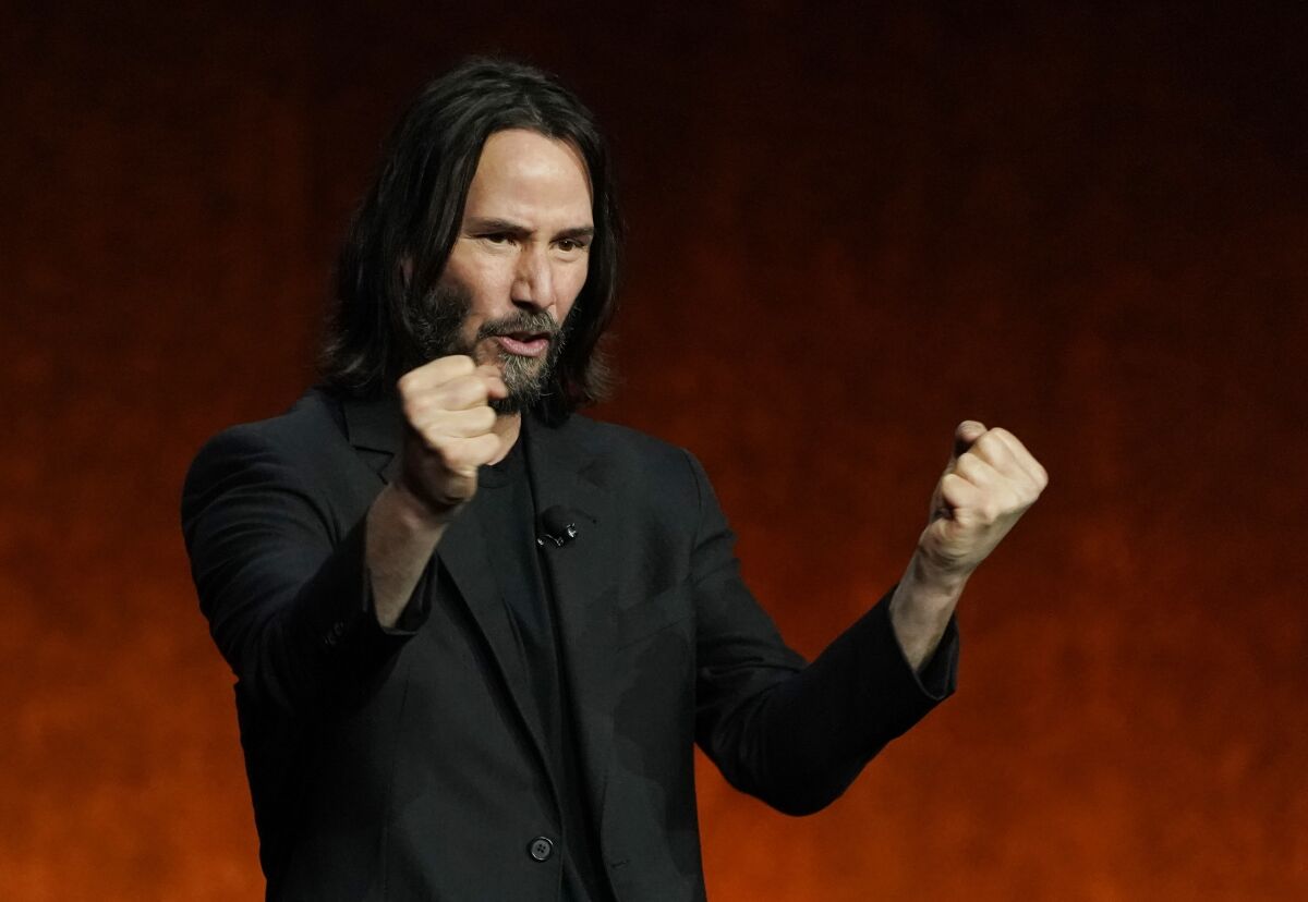 Man with long hair and wearing a black blazer and shirt, clenches his fists on stage