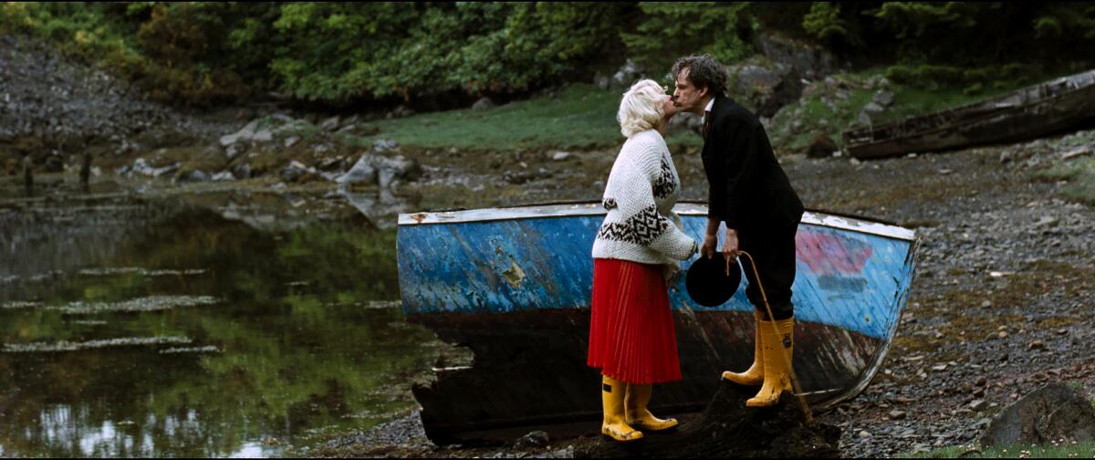 A blonde and a man in a suit kiss on a beach.