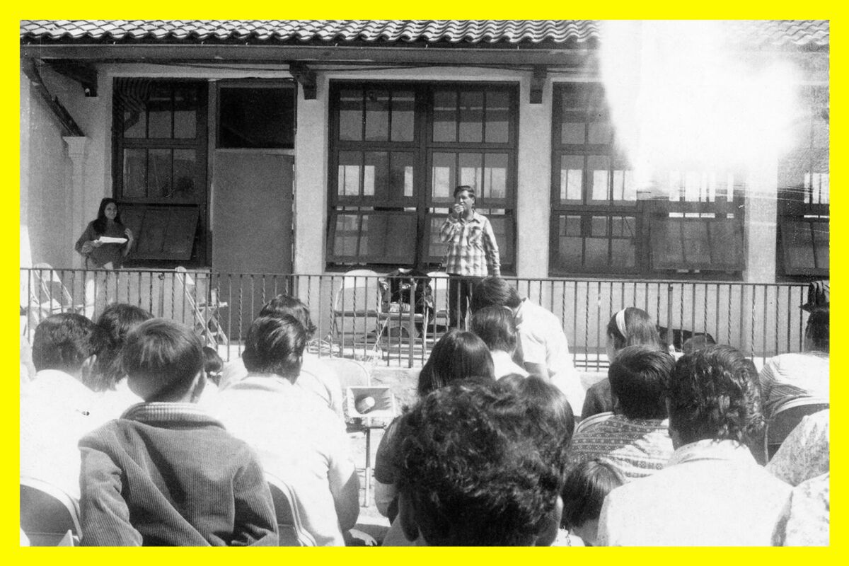 A man stands on a porch, speaking to a group of people.