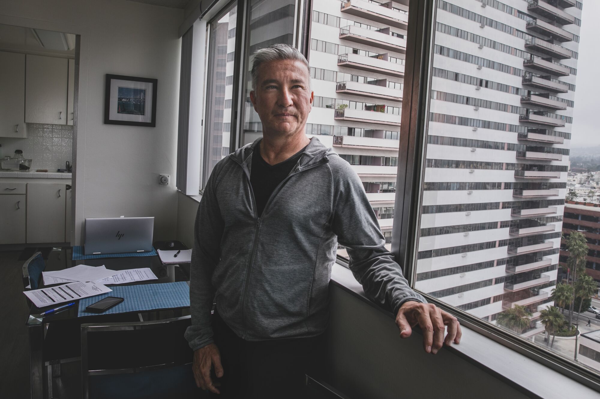 A man stands at a window inside an apartment.