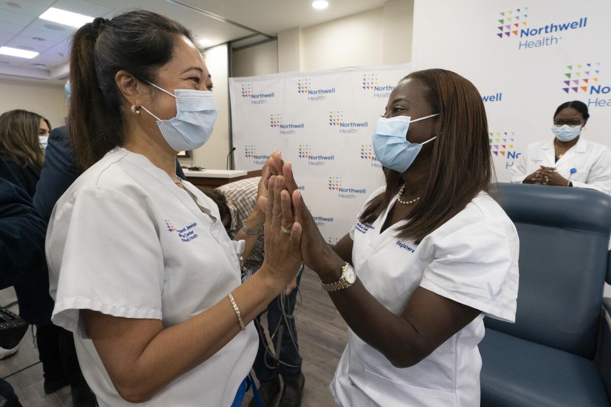 Two nurses wearing masks face each other and hold their hands up against the other's.