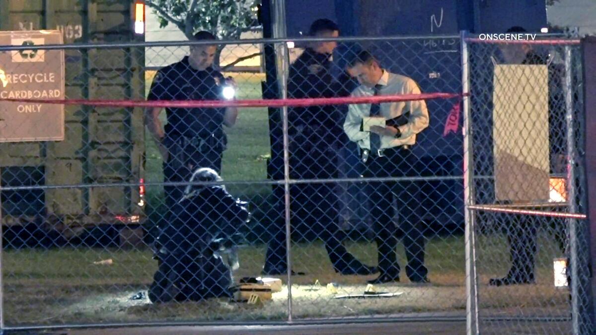 A few police officers and a man in a shirt and tie standing behind a chain-link fence.