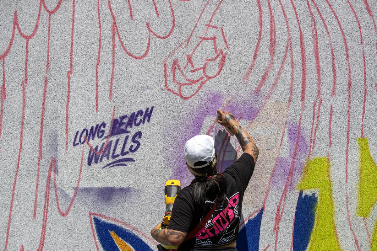 Long Beach Walls artist Stevie Shao sprays paint on a mural in progress.