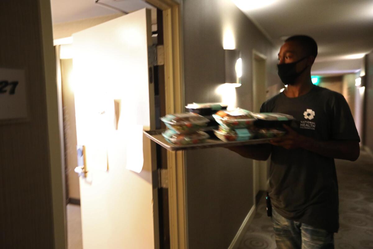 Guest services associate Jon Crosby, 27, carries a tray of lunches for guests at a Project Roomkey hotel in Los Angeles.