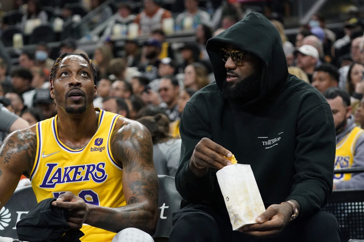 Los Angeles Lakers forward LeBron James, right, talks with teammate Dwight Howard, left, and eats a snack while on the bench during the first half of an NBA basketball game against the San Antonio Spurs, Monday, March 7, 2022, in San Antonio. James did not play. (AP Photo/Eric Gay)