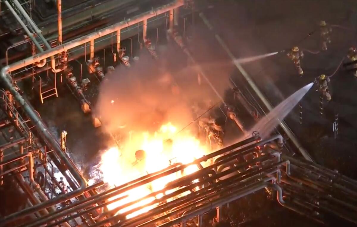 Aerial view of firefighters spraying water on flames burning in an oil refinery.