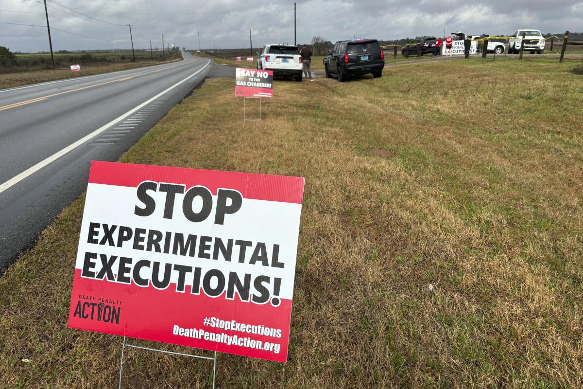 A sign reading "Stop experimental executions!" stands next to a road
