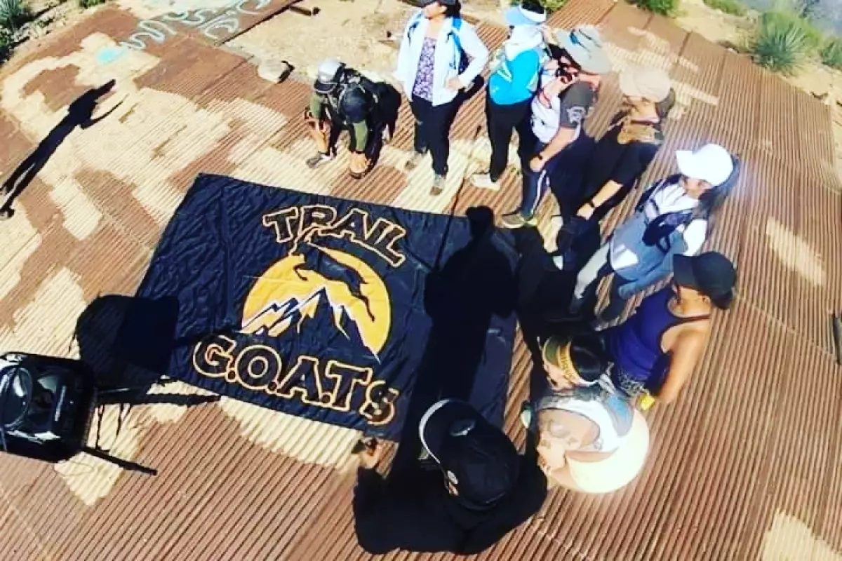 Runners stand around a banner on the ground that says Trail Goats