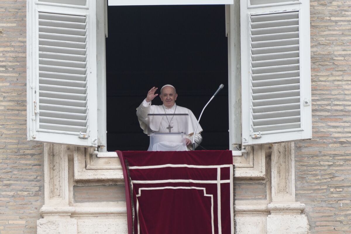 Pope Francis stands at a window with its shutters thrown open.