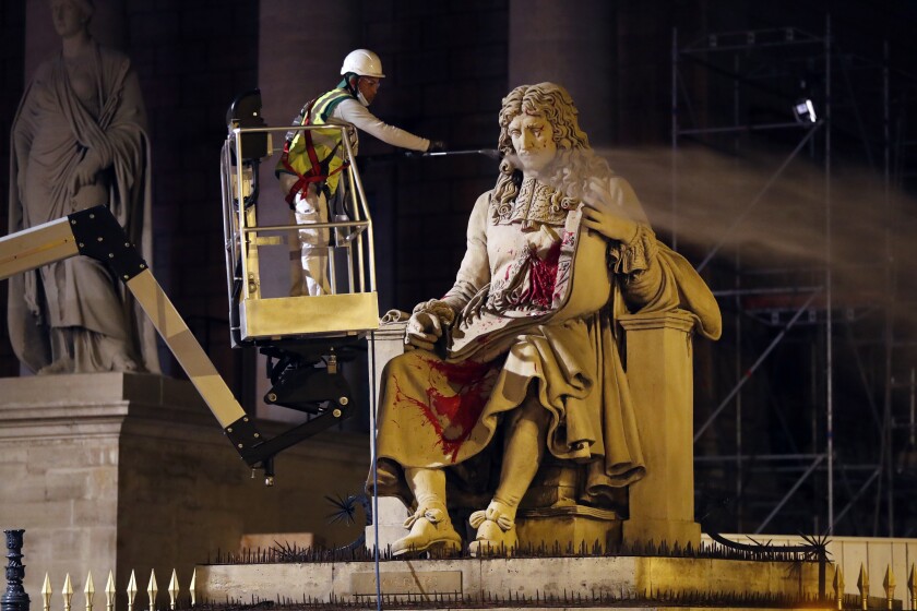 FILE - In this June 23, 2020 file photo, a worker from Paris' City Hall cleans the statue of Jean-Baptiste Colbert, in Paris. Trial began on Monday for Franco Lollia, an activist from a group called the Anti-Negrophobia Brigade, who stands accused of covering in graffiti a statue that honours Jean-Baptiste Colbert, a 17th century royal minister who wrote rules governing slaves in France's overseas colonies and stands in front of the National Assembly, a prominent landmark overlooking the Seine River in Paris. (AP Photo/Thibault Camus, File)