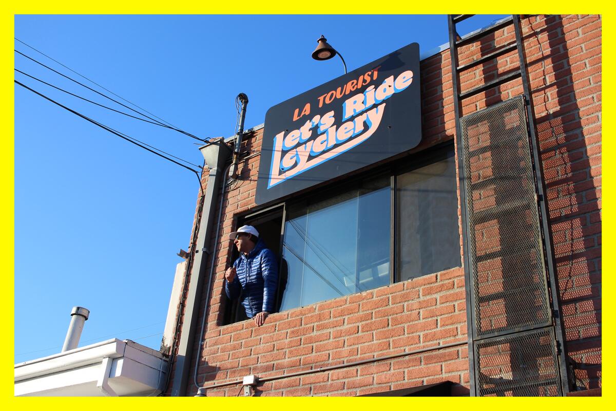 A man looks out of a second story window beneath the Let's Ride Cyclery sign