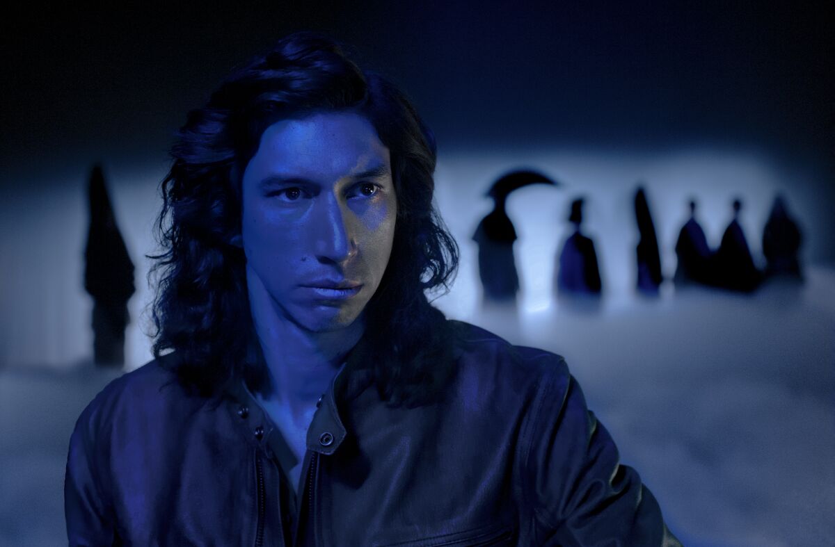 A man with shoulder-length hair in dark lighting